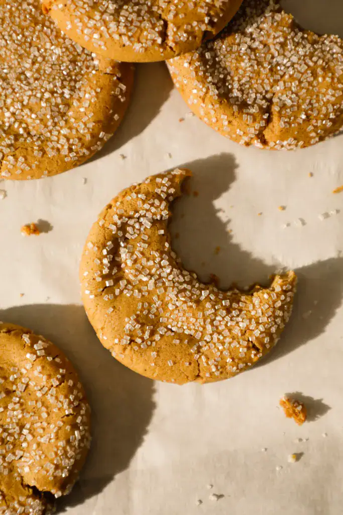 Chewy ginger cookie with coarse sugar topping and a bite missing, showing soft inside texture