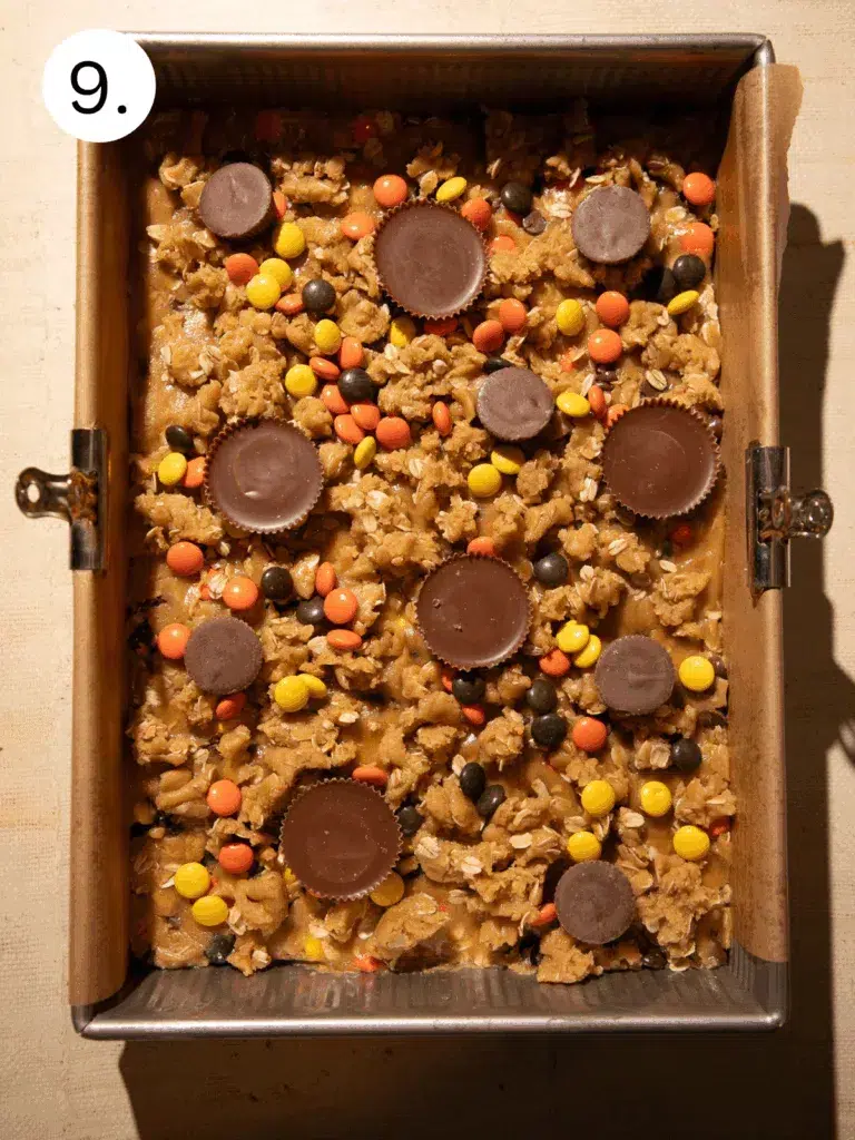 Scooping and pressing monster cookie dough with Reese’s candy into a baking pan
