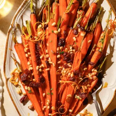 Overhead view of roasted honey glazed carrots topped with dried cranberries, toasted pine nuts, and orange zest on a serving platter.