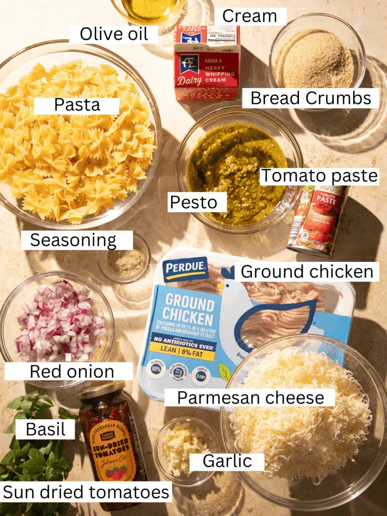 Overhead view of ingredients for marry me chicken meatball pasta with basil pesto, including pasta, ground chicken, cream, pesto, parmesan, and sun-dried tomatoes.
