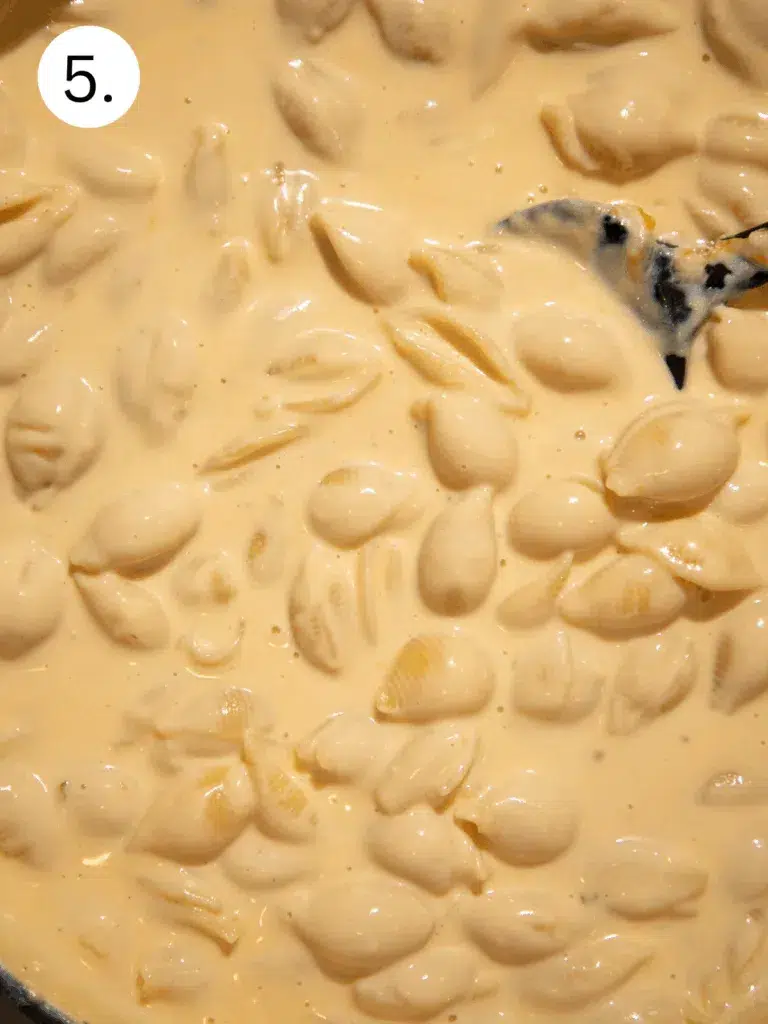 Overhead of a pot filled with cheesy pasta shells coated in thick sauce, stirred with a wooden spoon.