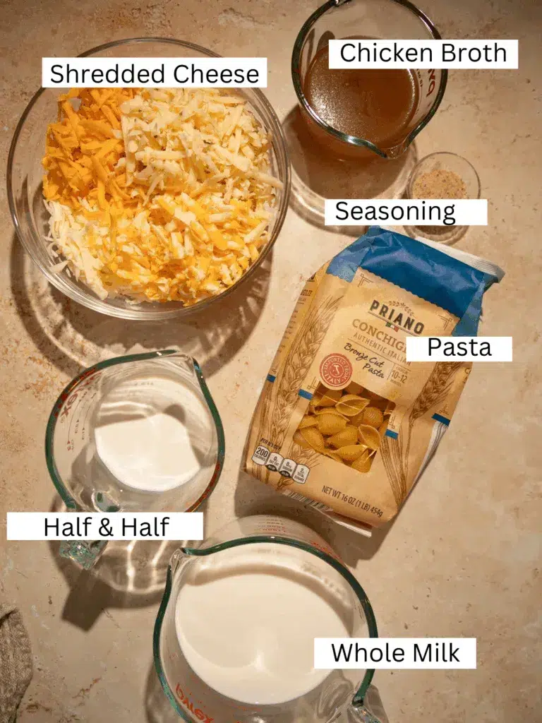 Overhead view of pasta shells, shredded cheese, milk, half and half, chicken broth, and seasonings arranged on a counter.