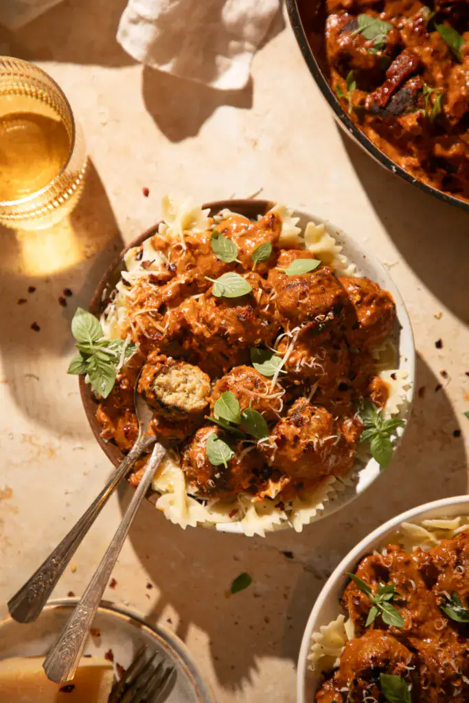 Bowl of creamy pesto marry me chicken meatballs with pasta, one meatball cut open to show juicy inside.