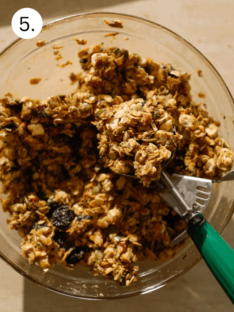 Mixing bowl with oat, nut, and dried fruit mixture being scooped for no-bake breakfast cookies.