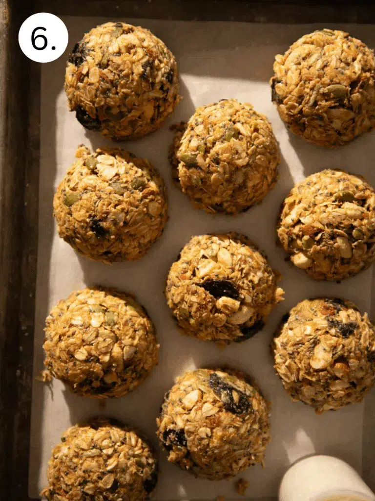 Scooped no-bake breakfast cookies with oats, seeds, and dried cherries arranged on a parchment-lined baking sheet.