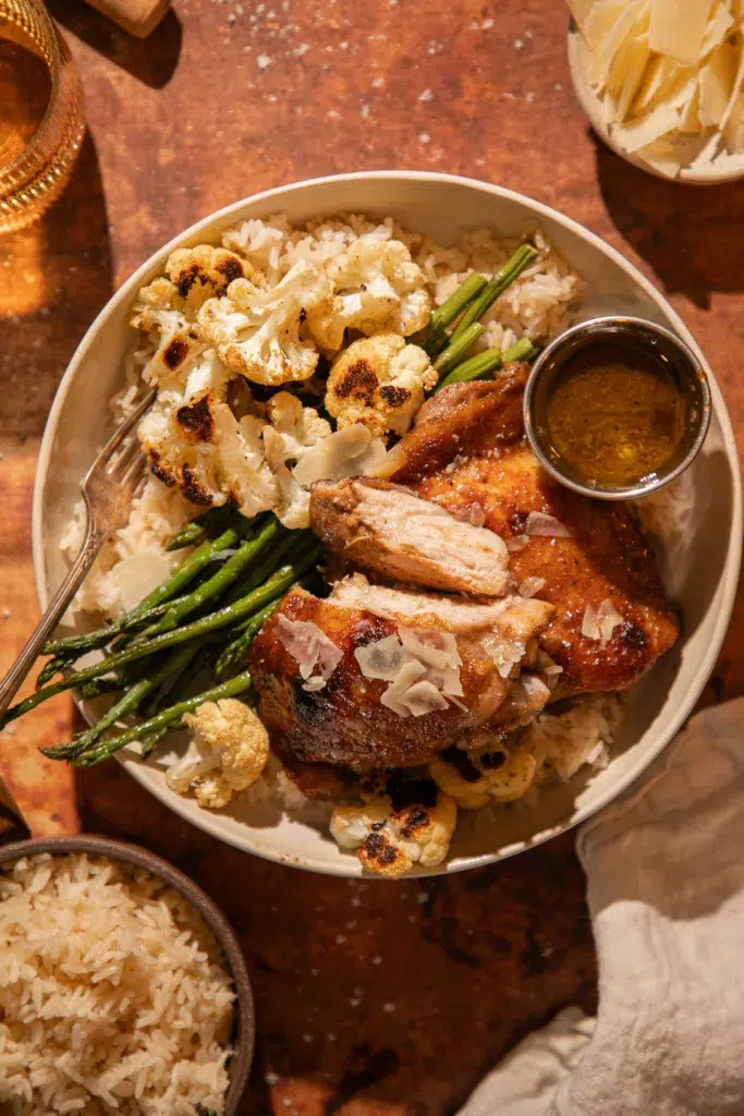 Close-up of roasted chicken thighs with golden, caramelized balsamic glaze and parmesan shavings.