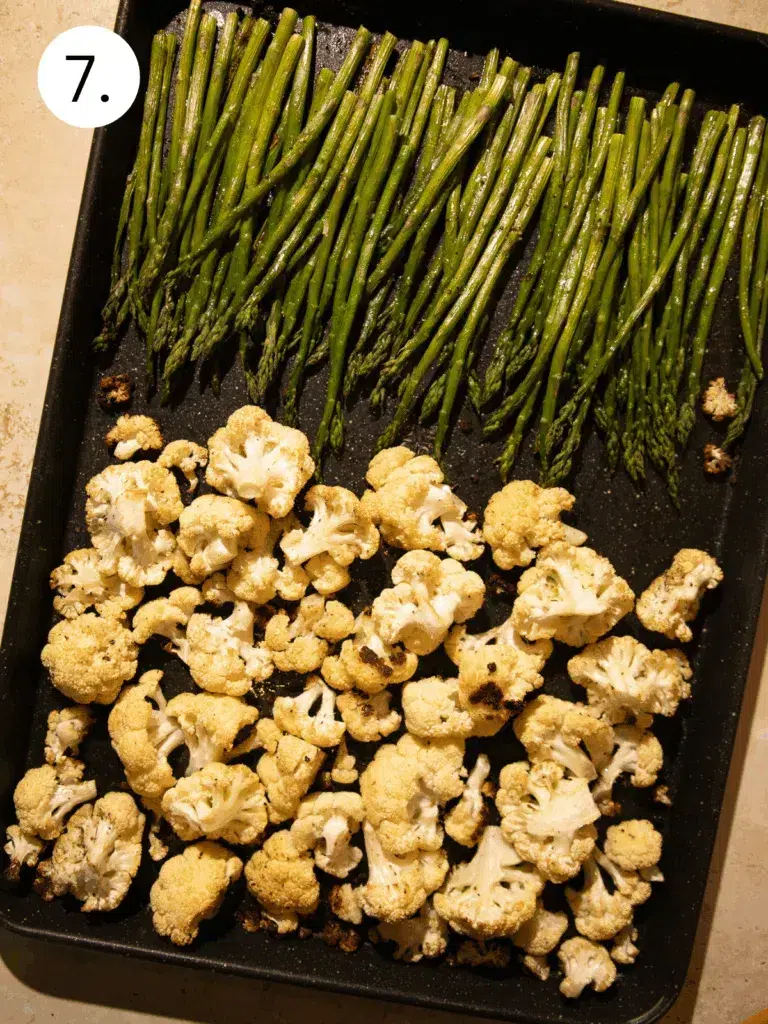 Golden roasted cauliflower and tender asparagus on a black sheet pan.