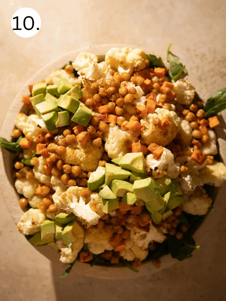 Large bowl of roasted cauliflower salad with sweet potatoes, crispy chickpeas, avocado, arugula, and parmesan with lemon tahini dressing.