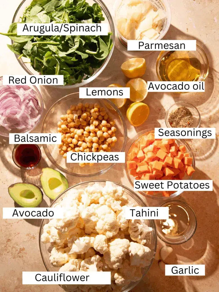 Ingredients for roasted cauliflower salad including cauliflower, sweet potatoes, arugula, chickpeas, avocado, parmesan, and tahini dressing.