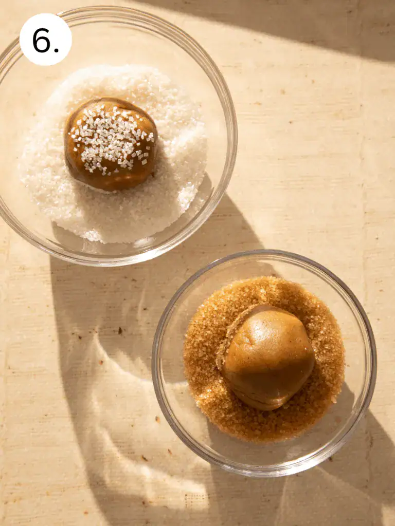 Scoops of ginger cookie dough lined up on a baking sheet before rolling in sugar.