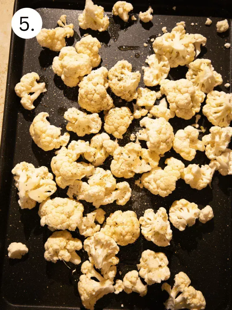 Raw cauliflower florets spread on a sheet pan, drizzled with olive oil and seasoning before roasting.