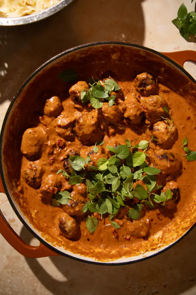Juicy chicken meatballs simmered in creamy sun-dried tomato marry me sauce, topped with fresh basil leaves in a large skillet.