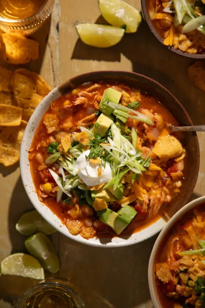 Close-up of chili filled with white beans, corn, shredded chicken, and topped with fresh cilantro, cheese, and crunchy chips.