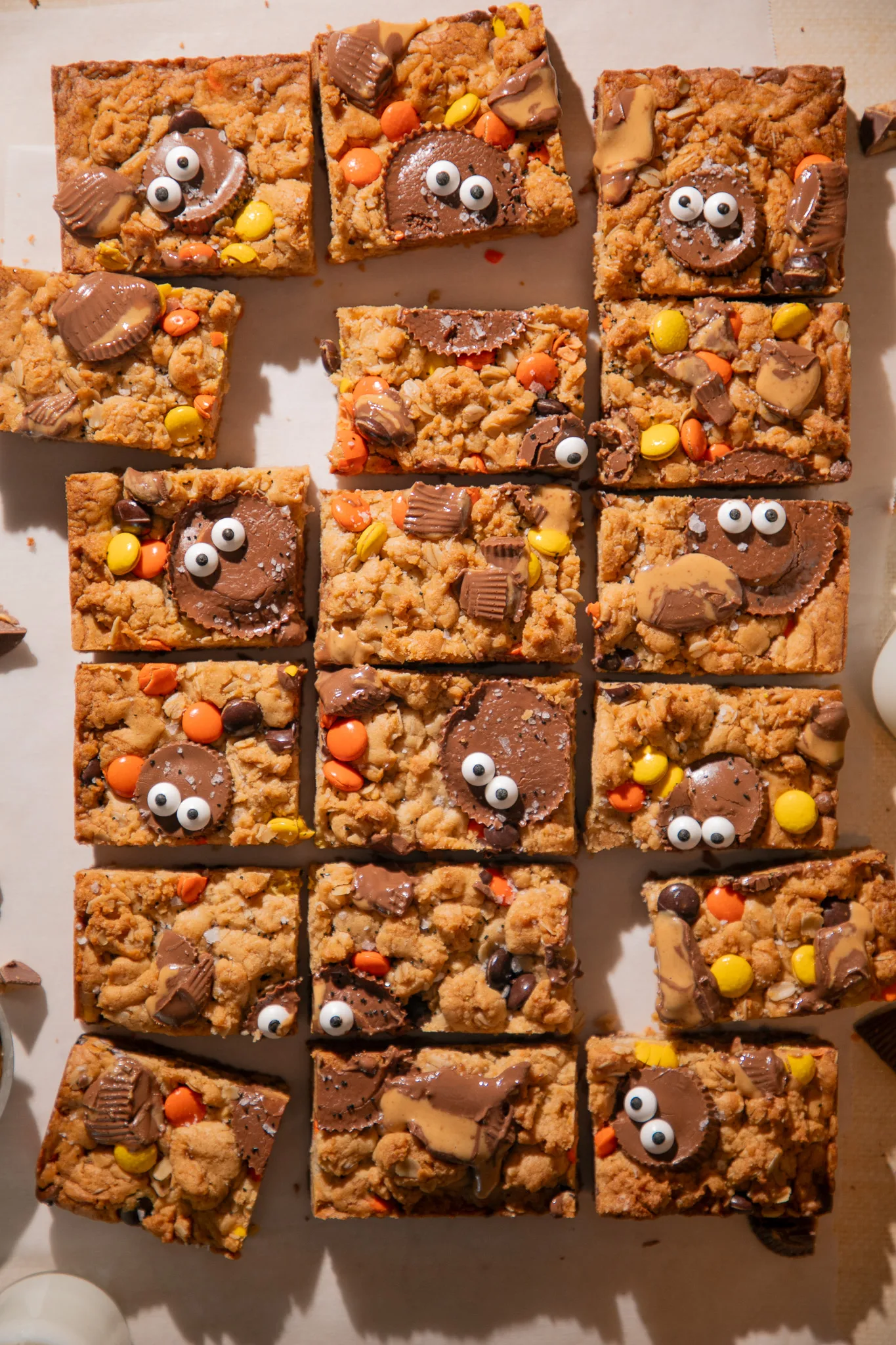 Rows of Halloween Reese’s Monster Cookie Bars with candy eyes, Reese’s Cups, and Reese’s Pieces, served with milk.