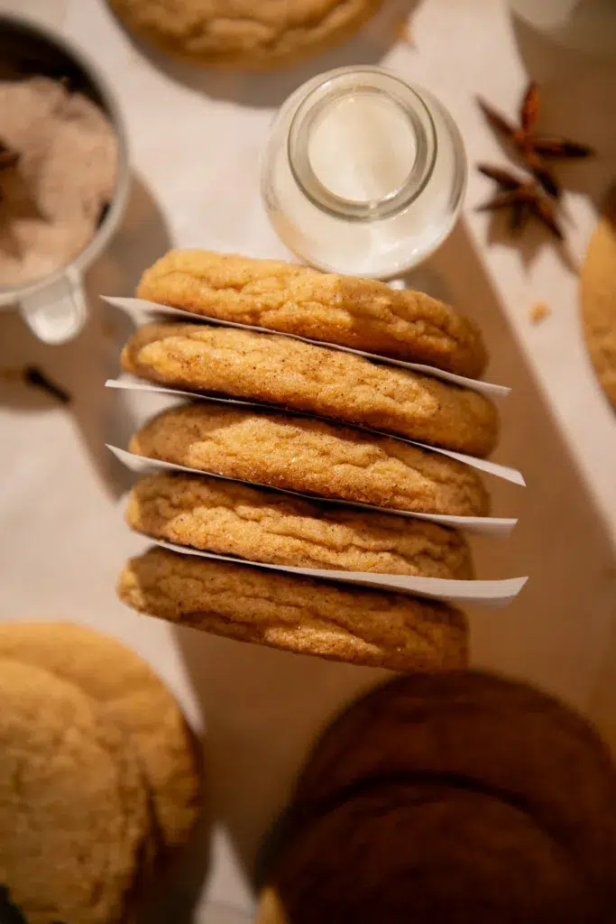 Stack of pumpkin chai snickerdoodles with parchment between layers and a small milk bottle.
