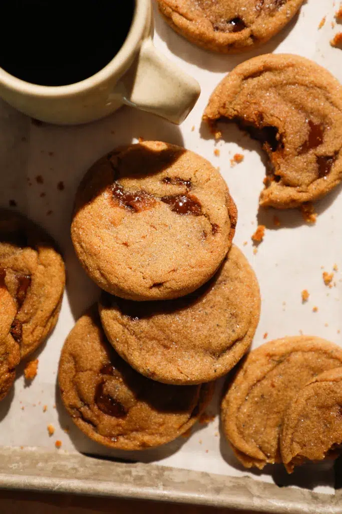 Brown butter brown sugar cookies with melted toffee pieces, stacked with coffee cup.