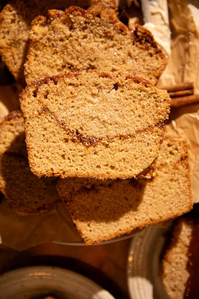 Thick slices of caramel apple cider donut bread stacked on parchment, showing cinnamon sugar swirl.