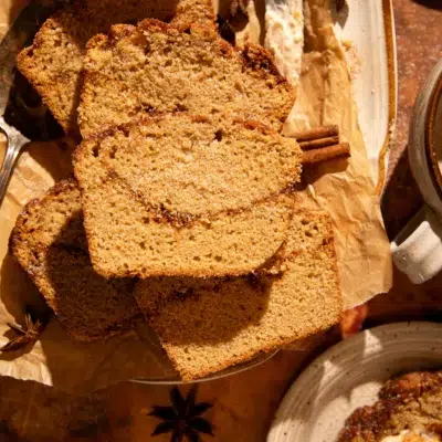 Overhead of apple cider donut bread slices styled with cinnamon sticks, maple butter, and a mug of coffee.
