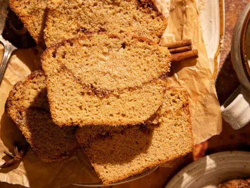 Overhead of apple cider donut bread slices styled with cinnamon sticks, maple butter, and a mug of coffee.
