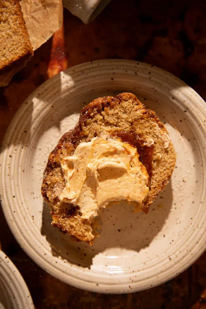 Slice of caramel apple cider donut bread with a bite taken out, topped with whipped maple butter.