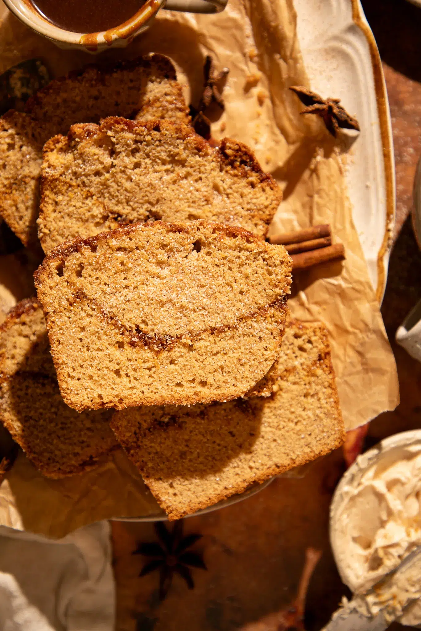 Close-up of sliced caramel apple cider donut bread with sugar crust, surrounded by spices and maple butter.