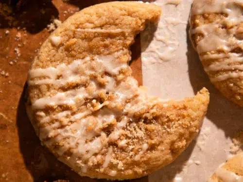 Glazed apple cider coffee cake cookie with bite missing on parchment paper with spices around.
