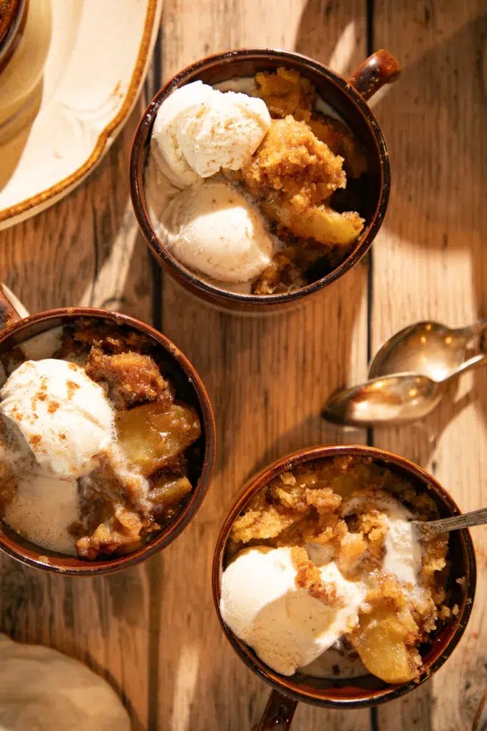 Overhead view of apple dump cake with melting ice cream scoops on wooden table