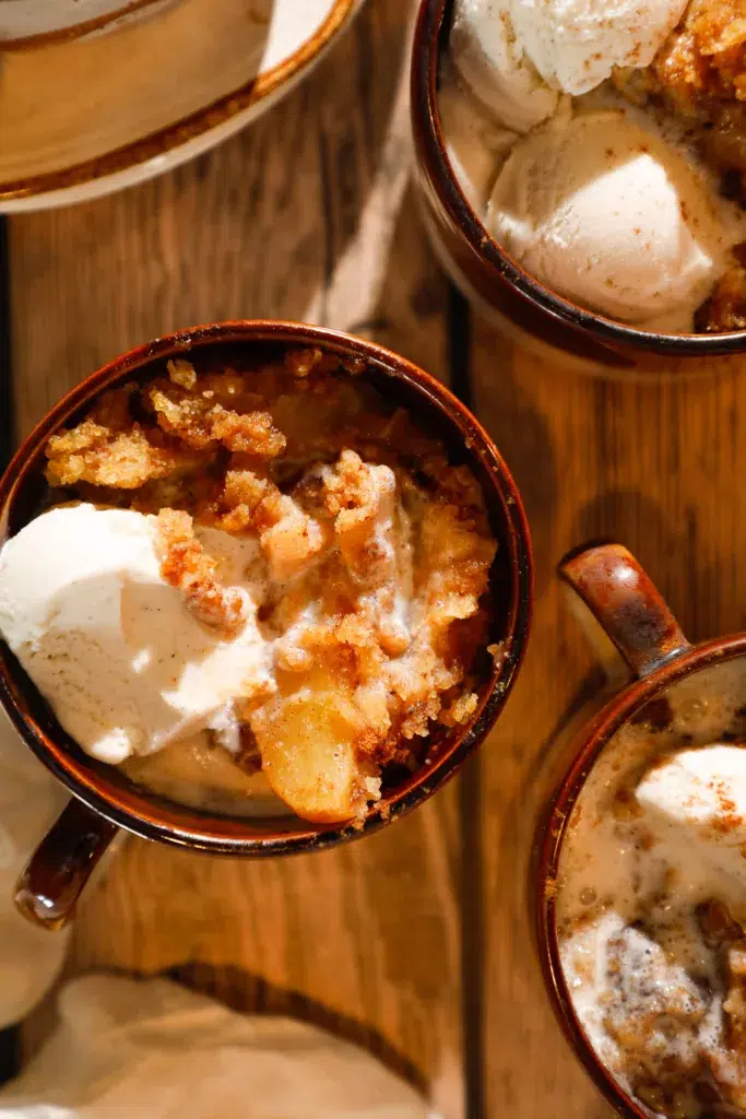 Rustic mugs filled with apple dump cake and vanilla ice cream ready to serve