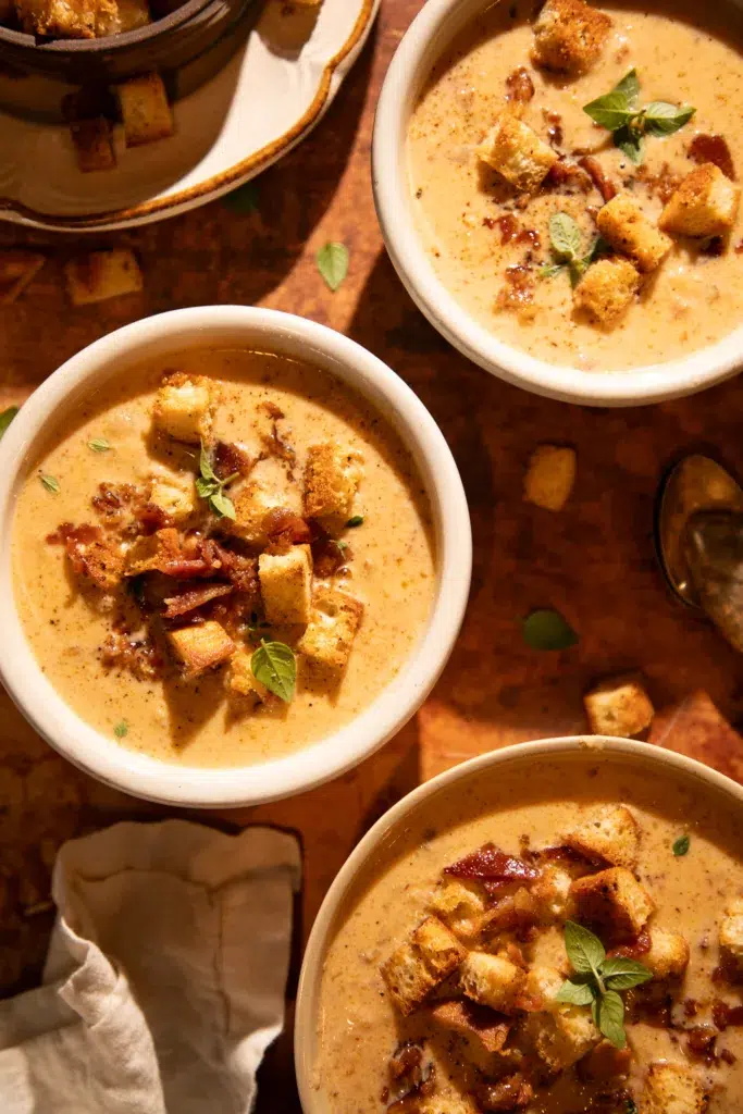 Thick creamy gouda cauliflower chowder in pot next to seasoned sourdough croutons on a baking sheet