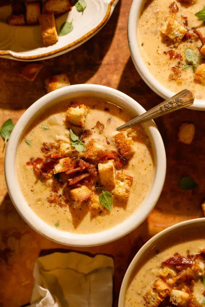 Close-up of rich smoky gouda cauliflower chowder with crispy bacon pieces, croutons, and fresh thyme