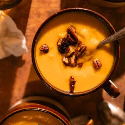 Multiple mugs filled with roasted butternut squash soup topped with toasted pecans.