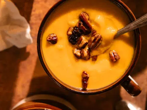 Multiple mugs filled with roasted butternut squash soup topped with toasted pecans.