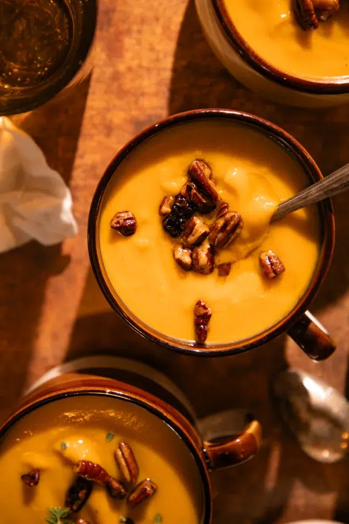Multiple mugs filled with roasted butternut squash soup topped with toasted pecans.