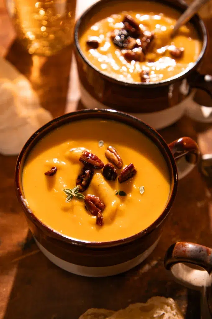 Close-up of creamy butternut squash soup garnished with toasted pecans and fresh thyme.