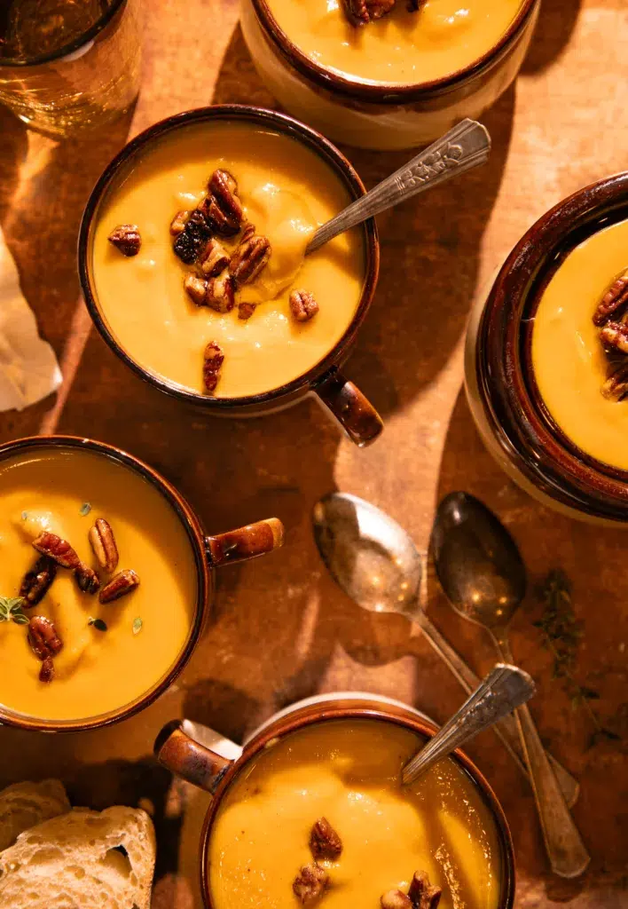 Creamy brown butter butternut squash soup topped with toasted pecans, served in mugs.