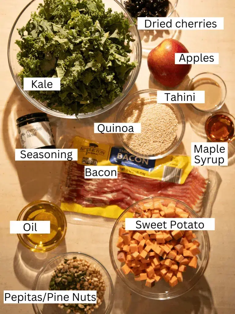 Overhead shot of kale, quinoa, sweet potatoes, bacon, apples, dried cherries, pepitas, pine nuts, tahini, and maple syrup laid out for a fall harvest salad.