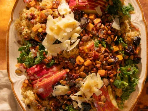 Close-up of autumn harvest salad with kale, quinoa, roasted sweet potatoes, apples, dried cherries, bacon, pepitas, pine nuts, and creamy bacon-tahini dressing.