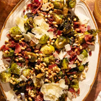 Close-up of Brussels sprouts with crispy bacon, pine nuts, and parmesan served on a platter.