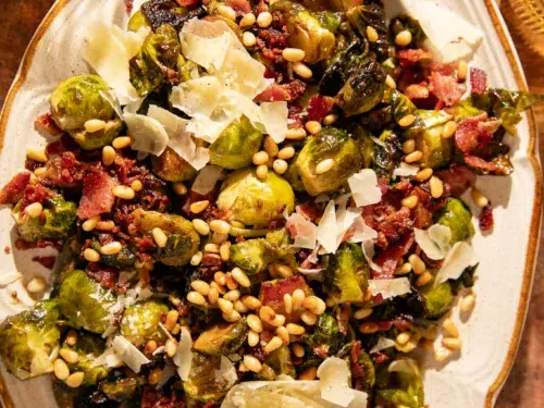 Close-up of Brussels sprouts with crispy bacon, pine nuts, and parmesan served on a platter.