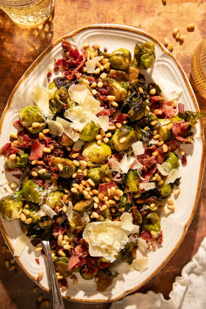Close-up of Brussels sprouts with crispy bacon, pine nuts, and parmesan served on a platter.