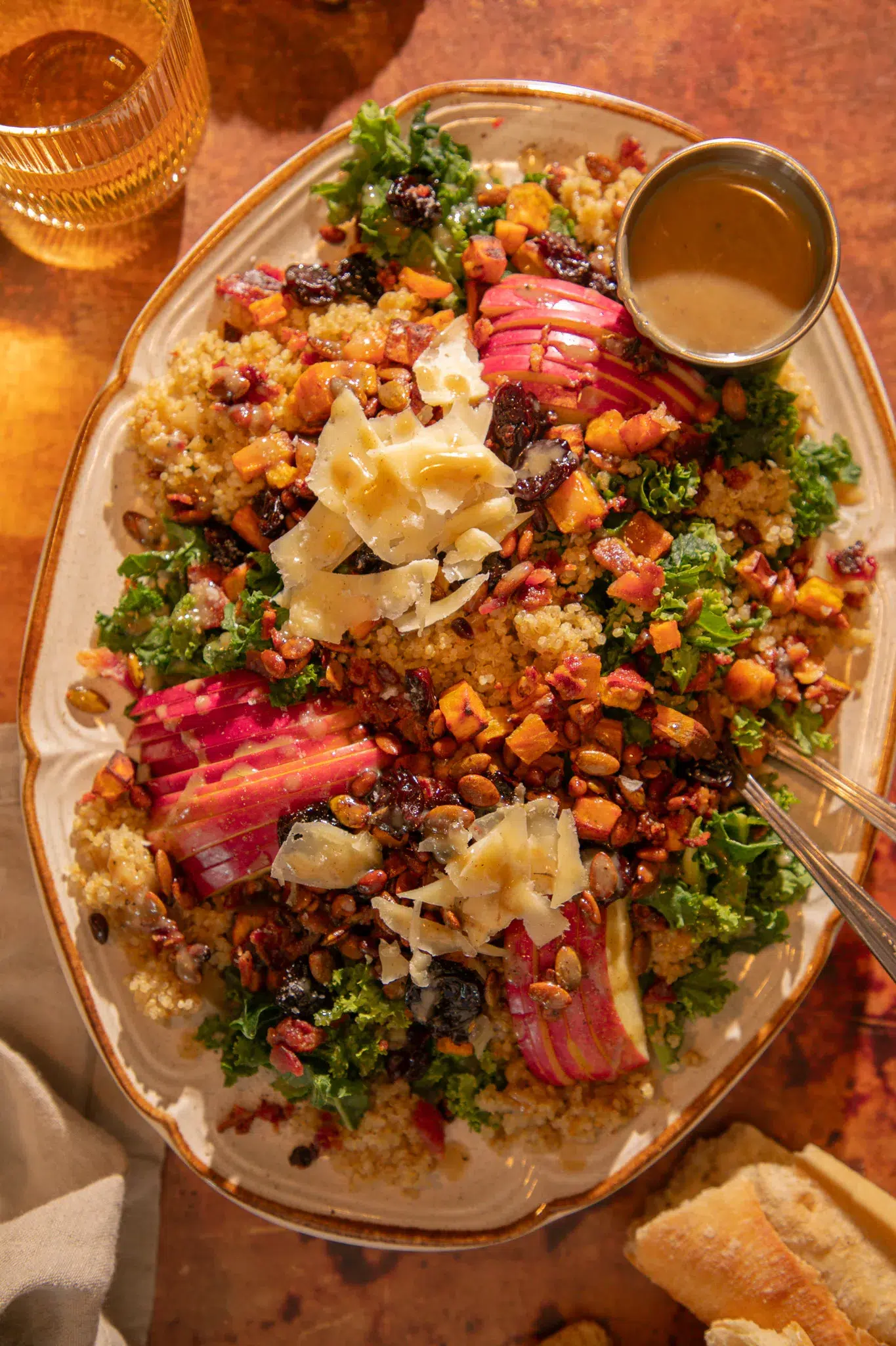 Large platter of fall harvest salad with kale, quinoa, roasted sweet potatoes, bacon, apples, dried cherries, pepitas, pine nuts, and shaved parmesan served with bacon-tahini vinaigrette.