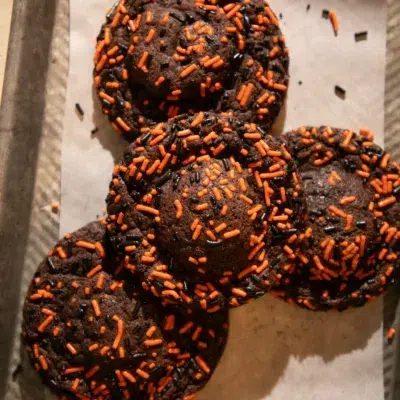 Stack of chocolate cookies stuffed with Oreos, decorated with orange and black sprinkles, one split open to reveal the Oreo inside.