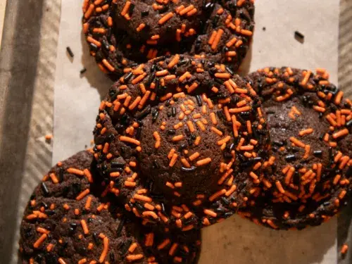 Stack of chocolate cookies stuffed with Oreos, decorated with orange and black sprinkles, one split open to reveal the Oreo inside.