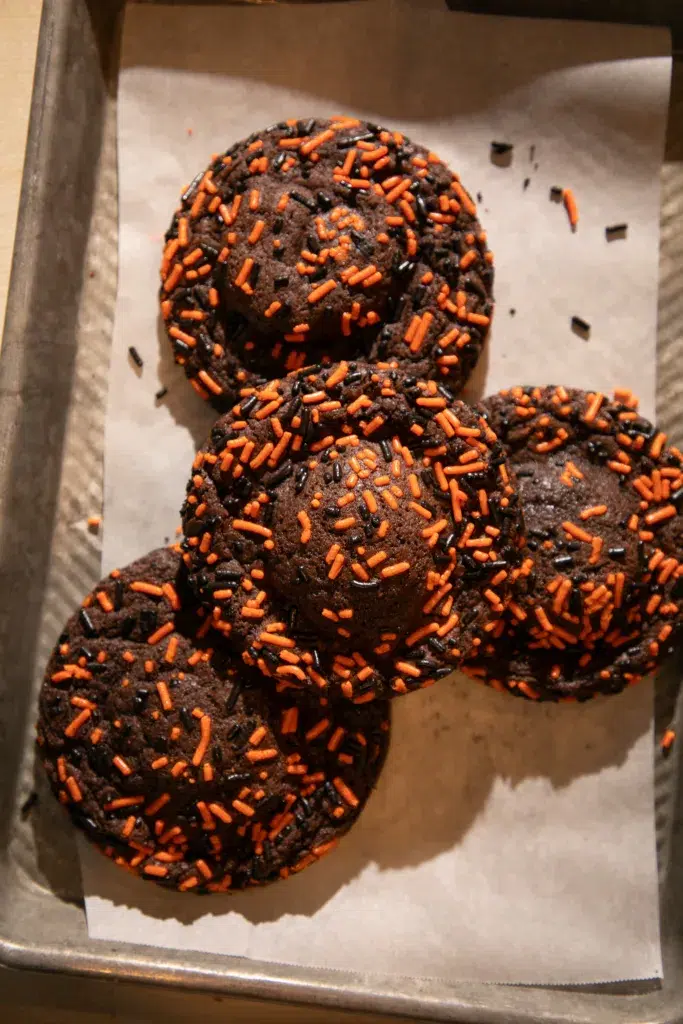 Stack of chocolate cookies stuffed with Oreos, decorated with orange and black sprinkles, one split open to reveal the Oreo inside.