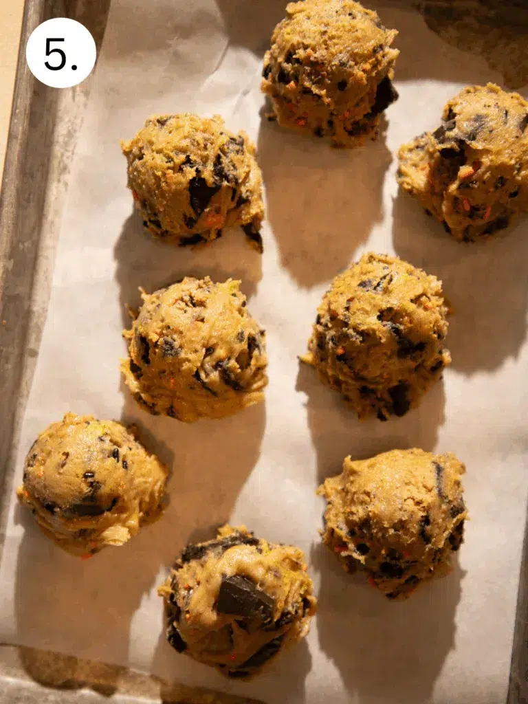 Scoops of cookie dough packed with Oreos, Reese’s, and sprinkles on a baking sheet.