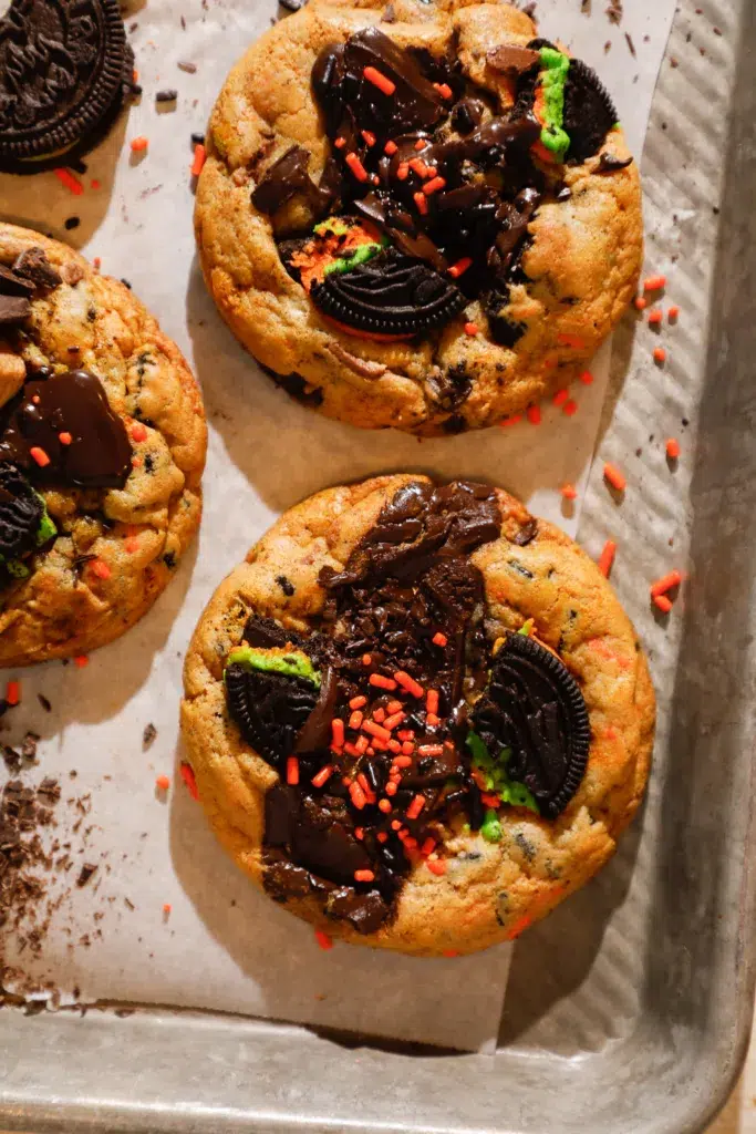 Close-up of one loaded Halloween chocolate chip cookie with melted chocolate and bright orange and black sprinkles.