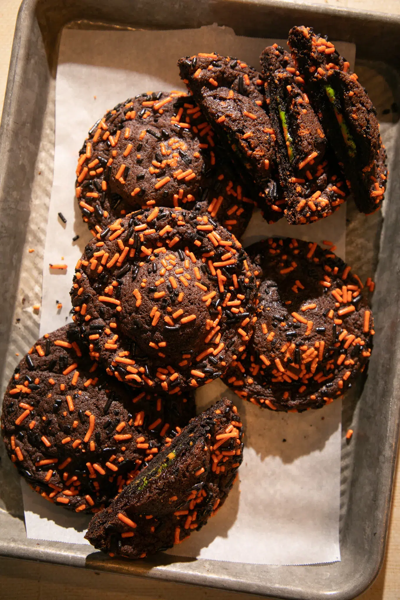 Large chocolate cookies topped with orange and black sprinkles cooling on a lined baking sheet.