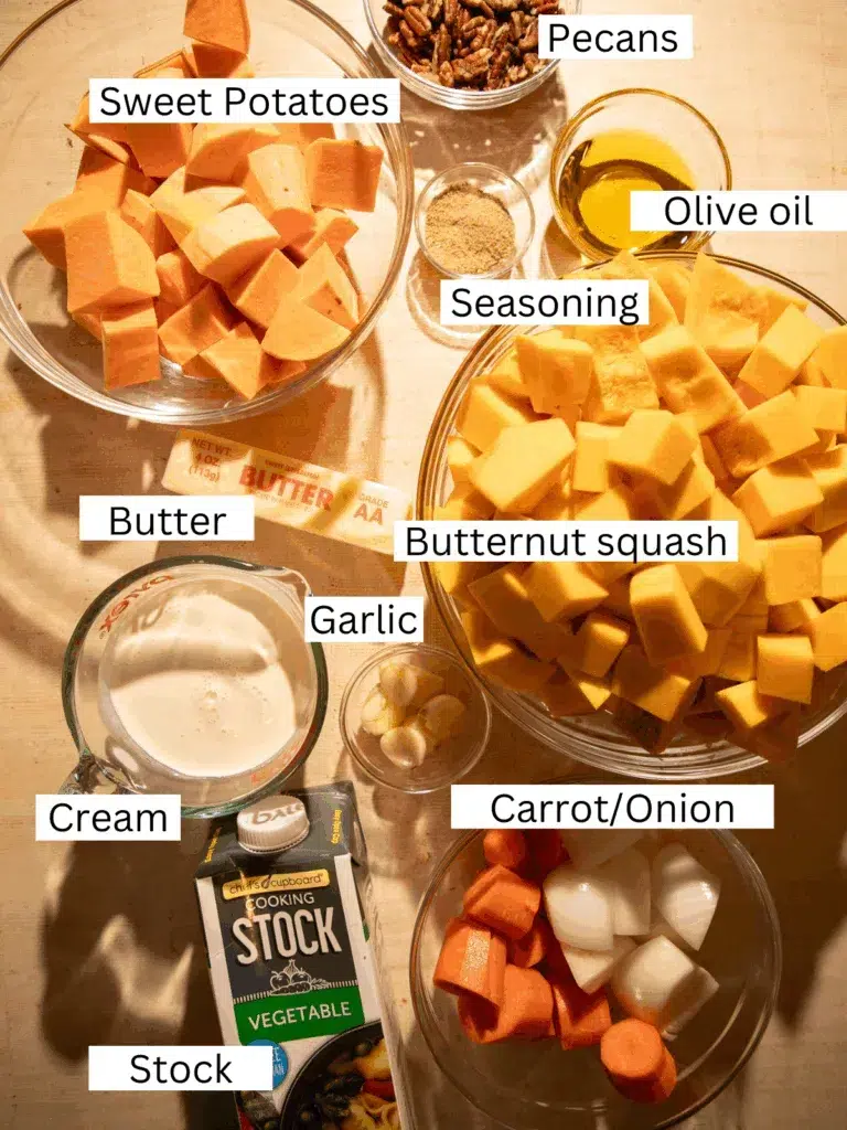 Overhead view of butternut squash soup ingredients including cubed squash, sweet potatoes, onion, garlic, carrots, pecans, cream, and vegetable stock.