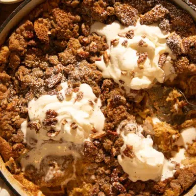 Pumpkin brioche French toast bake with pecans, partially scooped, showing soft custardy inside topped with whipped cream and streusel.