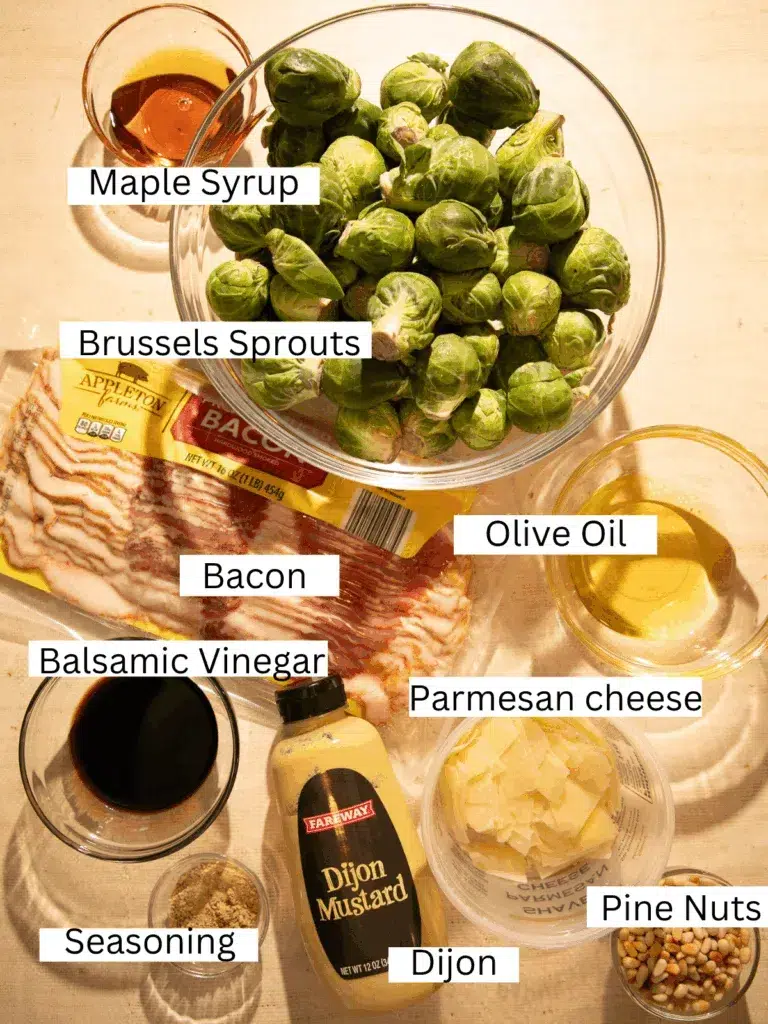 Overhead shot of fresh Brussels sprouts, bacon, pine nuts, parmesan, maple syrup, Dijon mustard, balsamic vinegar, olive oil, and seasonings on a countertop.